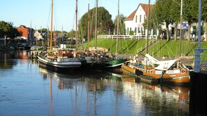 A marina with several boats docked, a white building with a red roof, and a grassy area with a white fence. - Apartment Schneider (Wittmund)