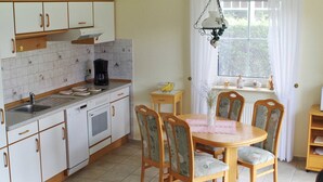 A kitchen with white cabinets, a coffee maker, a sink, and a dining table with chairs. - Apartment Schneider (Wittmund)