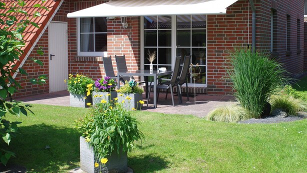 A patio with a table and chairs, surrounded by potted plants and a brick wall. - Apartment Schneider (Wittmund)