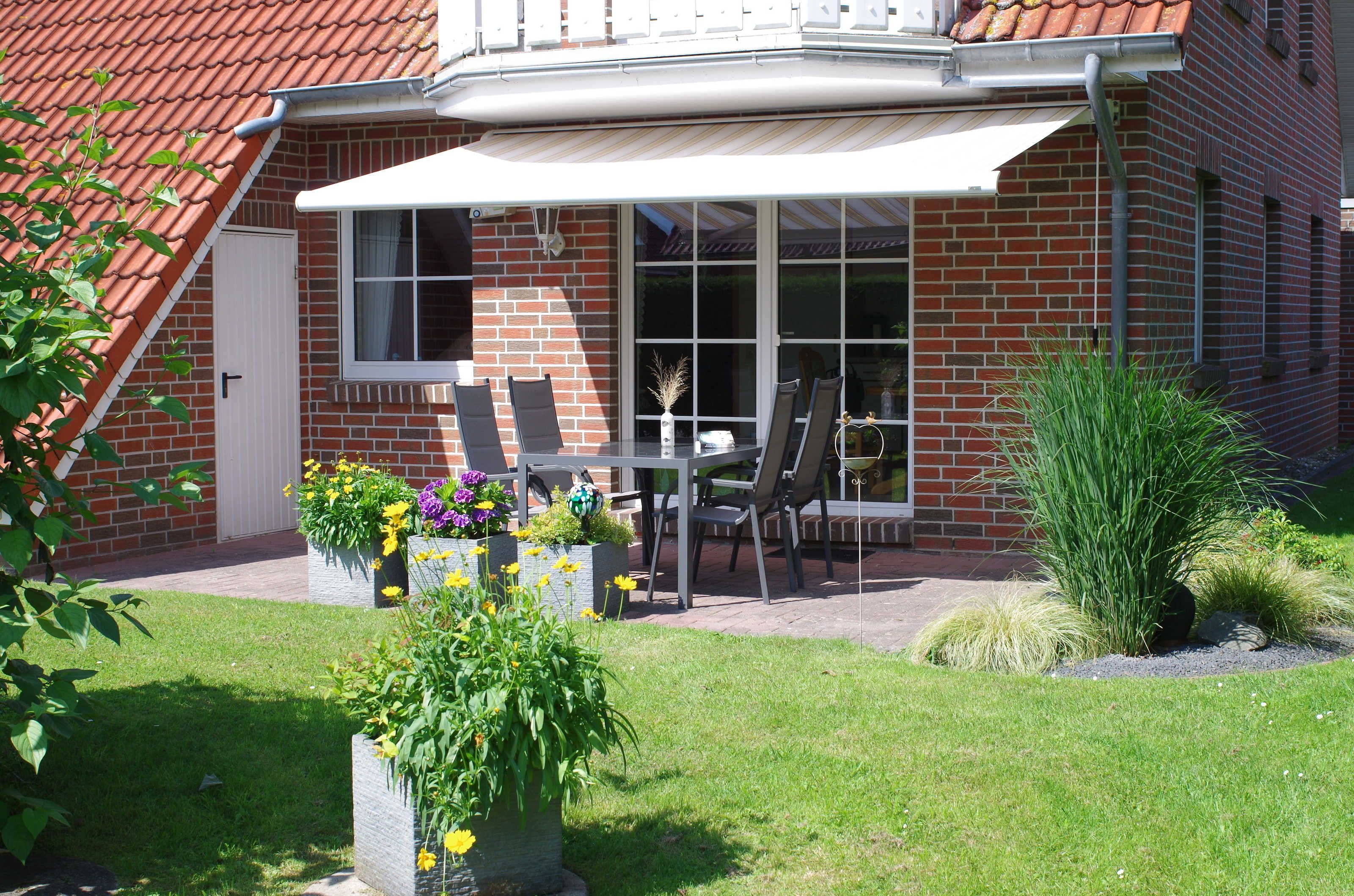 A patio with a table and chairs, surrounded by a brick wall and a white awning.