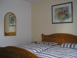 A bedroom with a wooden bed, a mirror, and two framed artworks on the wall.