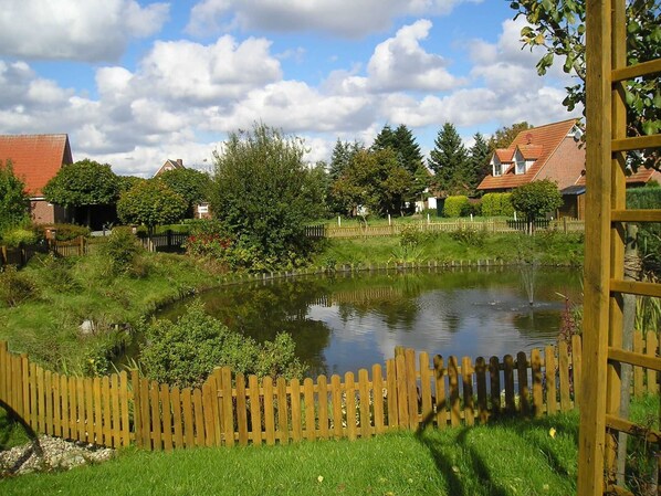 A pond with a wooden fence, surrounded by greenery and houses.