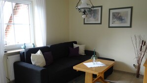 A living room with a black sofa, white and purple cushions, a wooden coffee table, and two framed artworks on the wall. - Apartment Schneider (Wittmund)