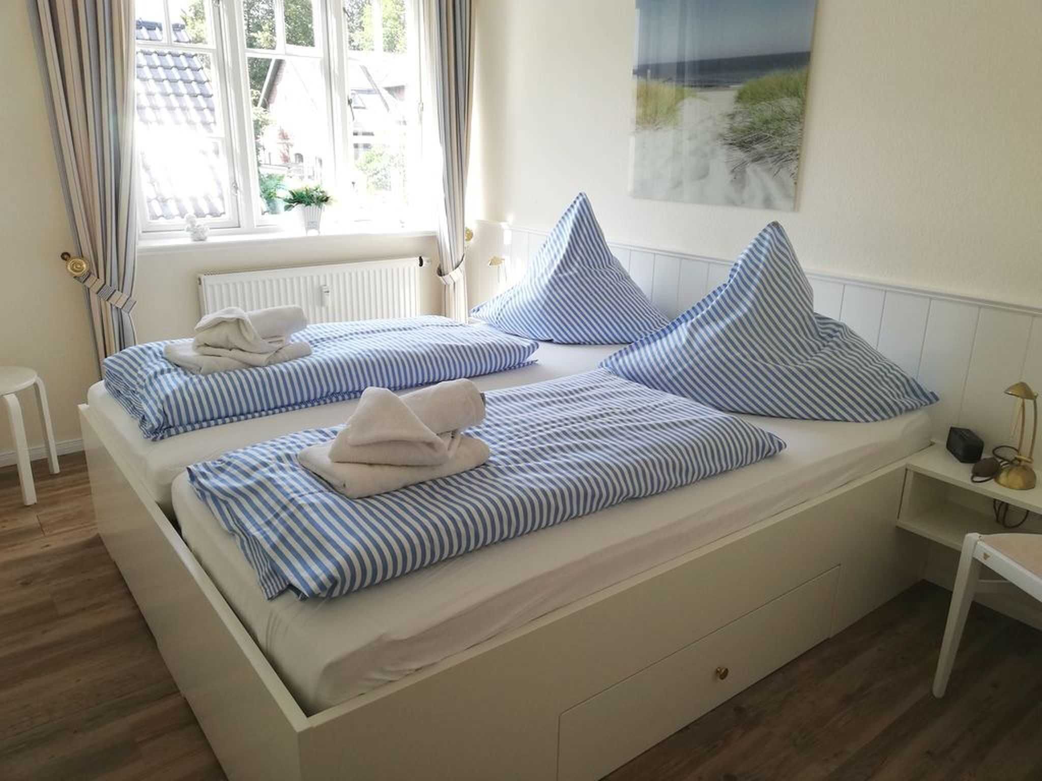 Ein Doppelbett mit gestreifter Bettwäsche, ein Nachttisch mit Lampe und ein Fenster mit Vorhängen.