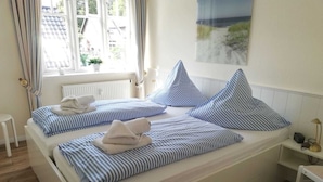 A double bed with striped bedding, a bedside table with a lamp, and a window with curtains. - Johannesstr. 12 apt. 4 (Wyk auf Föhr)