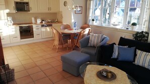 A modern kitchen with white cabinets, a dining area with wicker chairs, a sofa, and a glass coffee table. - Johannesstr. 12 apt. 4 (Wyk auf Föhr)