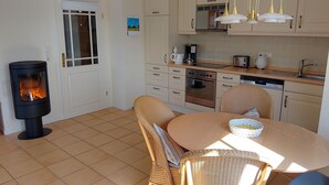 A cozy kitchen with a wood-burning stove, a dining table with chairs, and a window with a view. - Johannesstr. 12 apt. 4 (Wyk auf Föhr)