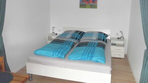 Un letto rifatto con lenzuola a righe blu e nere, due comodini con lampade e un quadro raffigurante un faro sulla parete.