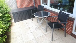 Un patio con un tavolo rotondo in vetro e due sedie, un muro in mattoni e una finestra che si affaccia sul quartiere.