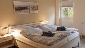 A neatly made bed with a patterned blanket, a bedside lamp, and a nightstand with a lamp. - Apple blossom house, Schmalstieg 1 (Wyk auf Föhr)