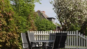 A patio with a table and chairs, surrounded by a white picket fence and lush greenery. - Apple blossom house, Schmalstieg 1 (Wyk auf Föhr)