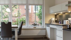 A modern kitchen with white cabinets, a built-in dishwasher, and a window overlooking a brick wall and greenery. - Apple blossom house, Schmalstieg 1 (Wyk auf Föhr)