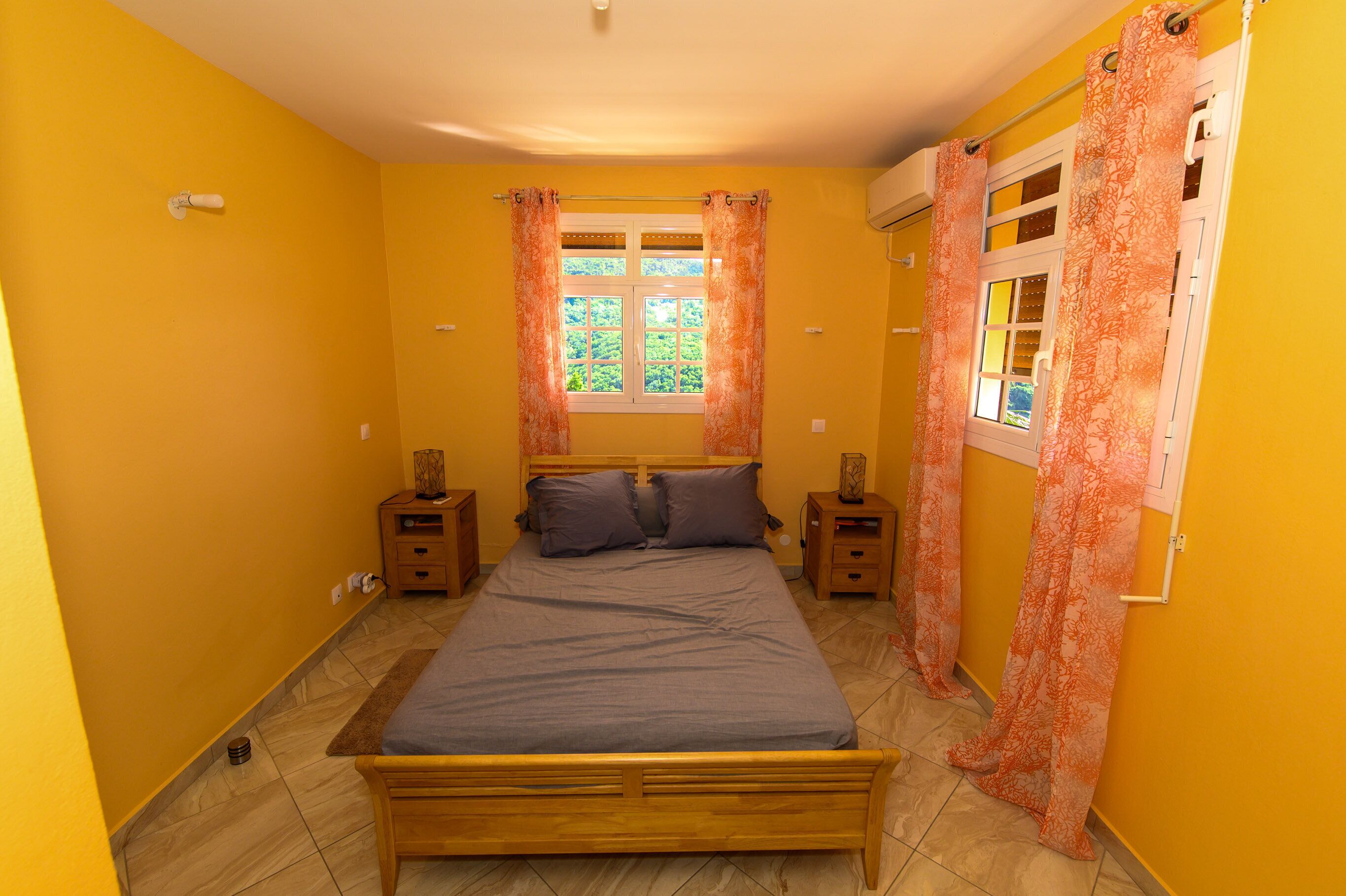 A bedroom with a bed, two bedside tables, a window with curtains, and a door with a mirror.