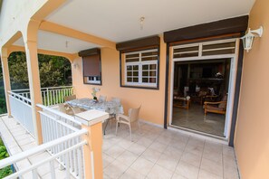 A balcony with a table and chairs, a sliding glass door leading to a living area, and a view of greenery. - Mountain view acomat pointe noire gp (pointe noire)