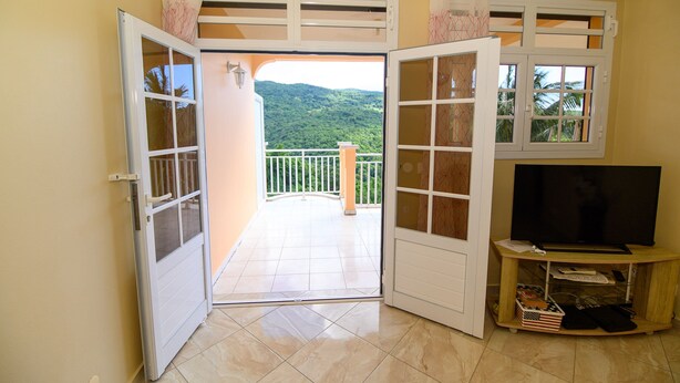 Ein Zimmer mit Fernseher, ein Balkon mit Blick auf grüne Hügel und eine Tür, die nach draußen führt.
