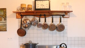 Eine Küche mit Herd, Backofen und hängenden Töpfen. Darüber befindet sich ein Regal mit Gläsern, auf denen 'Mehl' und 'Zucker' stehen.