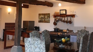 Ein rustikaler Essbereich mit hoher Holzbalkendecke, einer Steinwand und einer Küche mit hängenden Töpfen.