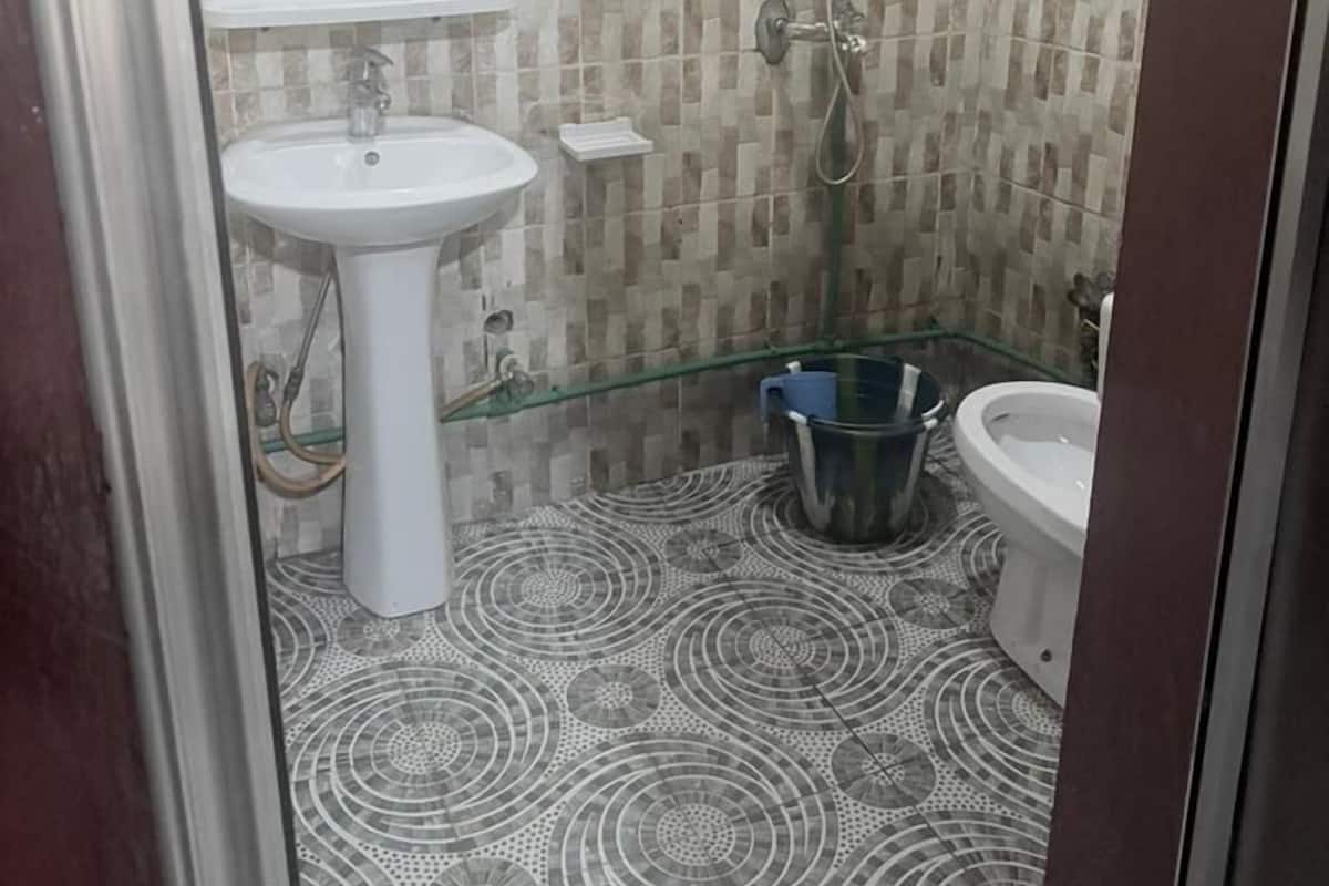 Um banheiro com pia branca, espelho redondo, chuveiro e bidê. O chão possui um desenho de azulejos estampados.