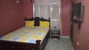 A bedroom with a bed, a bedside table with a water bottle, an air conditioner, and a television on a stand. - Hakaba (Conakry)