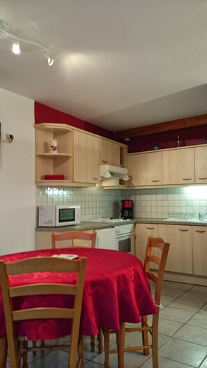 Een keuken met houten kastjes, een magnetron, een koffiezetapparaat en een eettafel met stoelen.