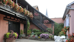 Um edifício tradicional com escadaria de madeira, caixas de flores e um pátio de tijolos com área de estar ao ar livre.