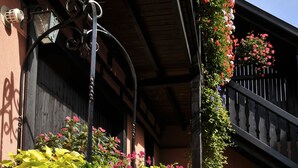 Um caminho de tijolos leva a um edifício com escadaria de madeira e uma caixa de flores com flores cor-de-rosa.
