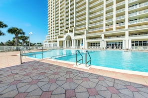A large hotel with multiple balconies, a swimming pool, and a paved walkway.