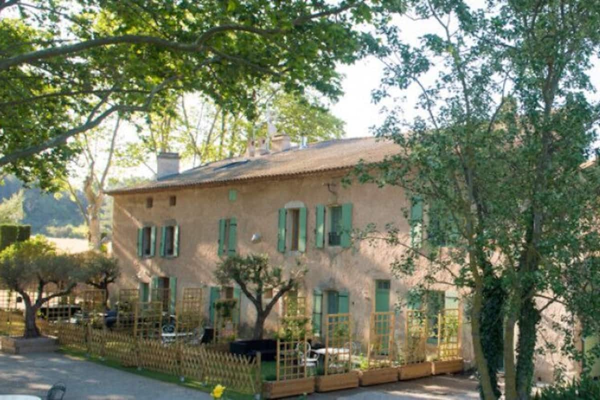 A rustic stone building with a traditional facade, a visible chimney, and a small garden area with a wooden fence.