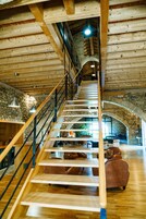 A wooden staircase leading to a stone-walled upper level with a seating area below.