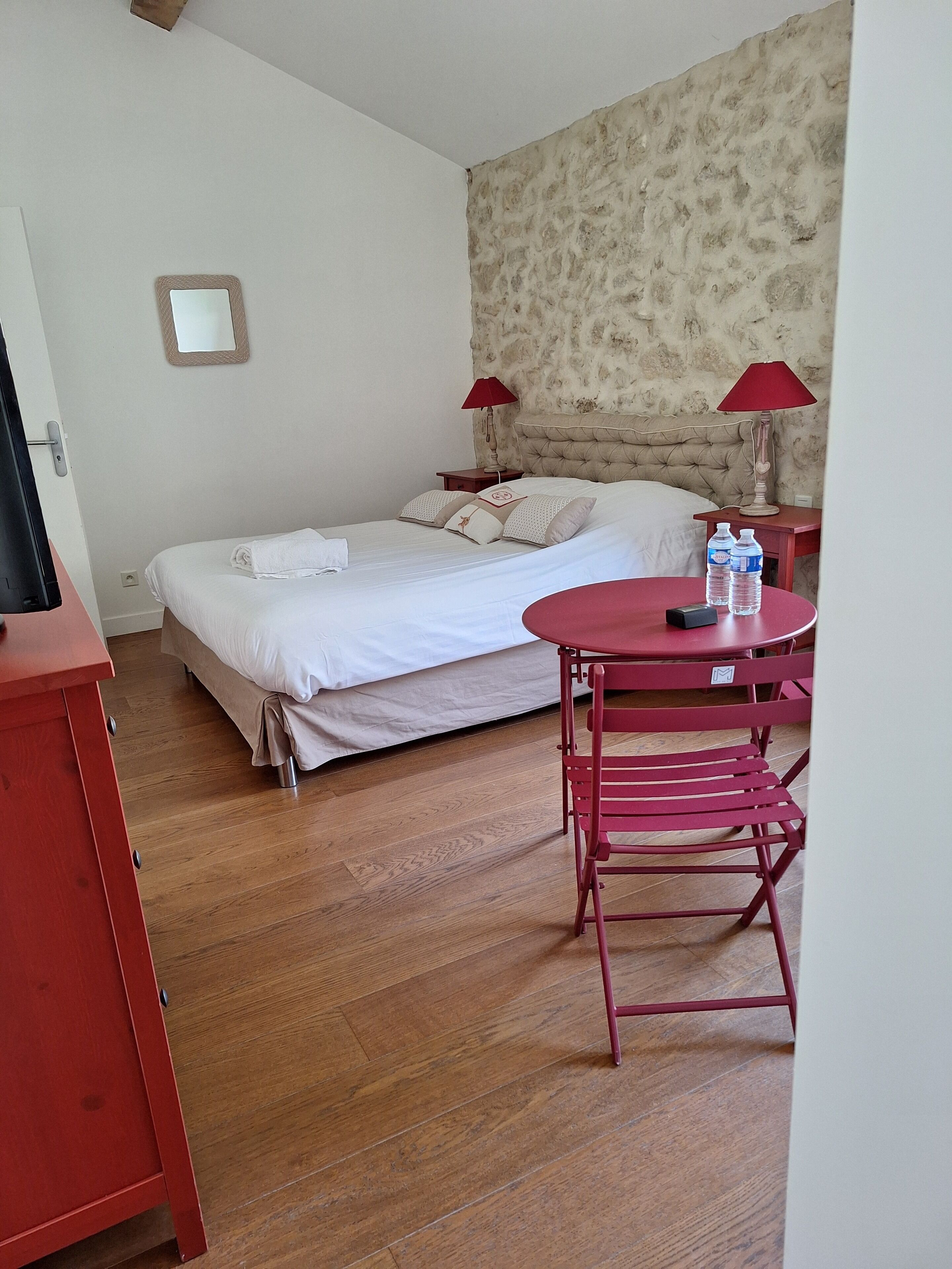 A bedroom with a bed, two bedside tables with lamps, a small table with water bottles, and a red chair.