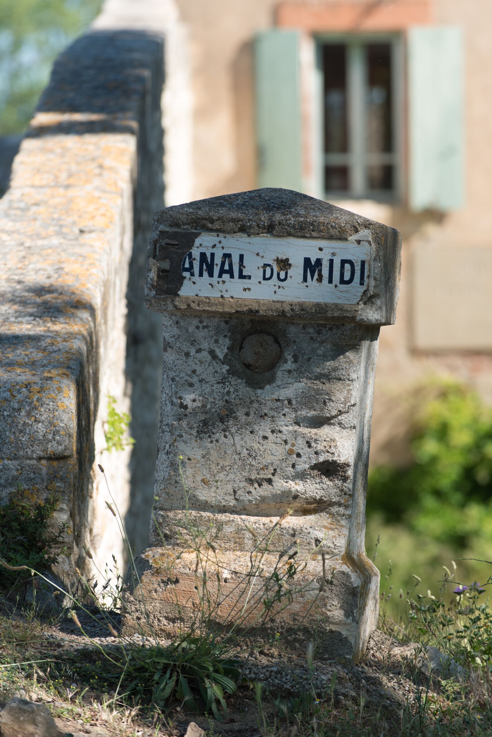 Um marcador de pedra desgastada com a inscrição 'ANAL DU MIDI' em ambiente rural.