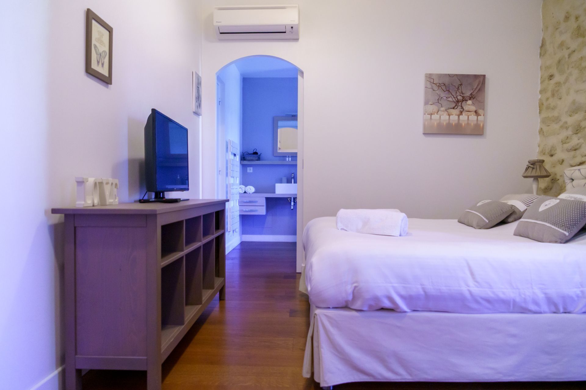 Hotelkamer met een bed, televisie, kledingkast, badkamer zichtbaar door een boog, en een schilderij aan de muur.