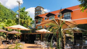 An outdoor seating area with umbrellas and chairs, a building with a sign reading "CLASSIC HOTEL", and a view of a hill with greenery. - Thermas Classic Hotel (Marcelino Ramos)