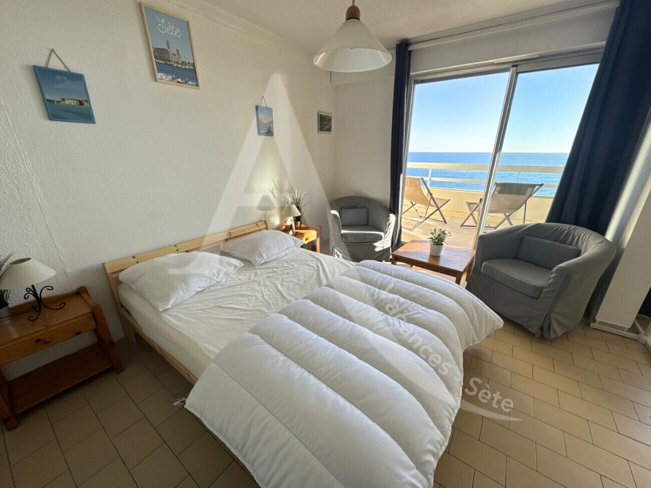 A bedroom with a bed, a chair, a small table, and a view of the beach.