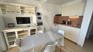 A compact kitchen with white cabinets, a microwave, a toaster, and a coffee maker. There is a dining table with a polka dot tablecloth and two chairs.
