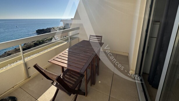 A balcony with a wooden table and chairs, overlooking the sea.