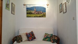 A bedroom with a bed, floral pillows, a framed picture of a building, and wall-mounted lights. - Detached house in a quiet private courtyard in the heart of Bergheim (Bergheim)