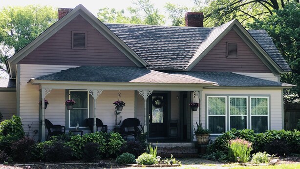 A two-story house with a porch, a front door, and a small garden area.