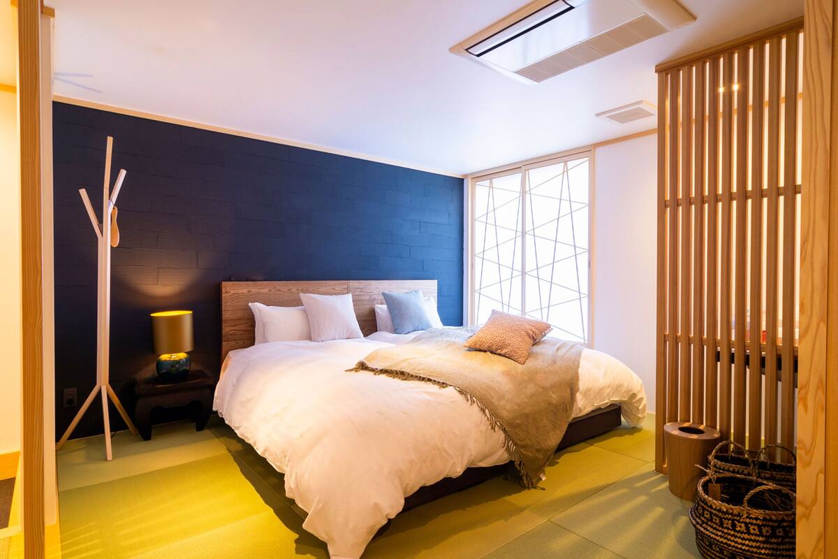 A modern bedroom with a large bed, a bedside lamp, a wooden floor, and a window with a view.