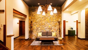 A spacious lobby with a stone wall, wooden flooring, a sofa with cushions, and a hanging light fixture. - Numajiri kogen lodge (Inawashiro)
