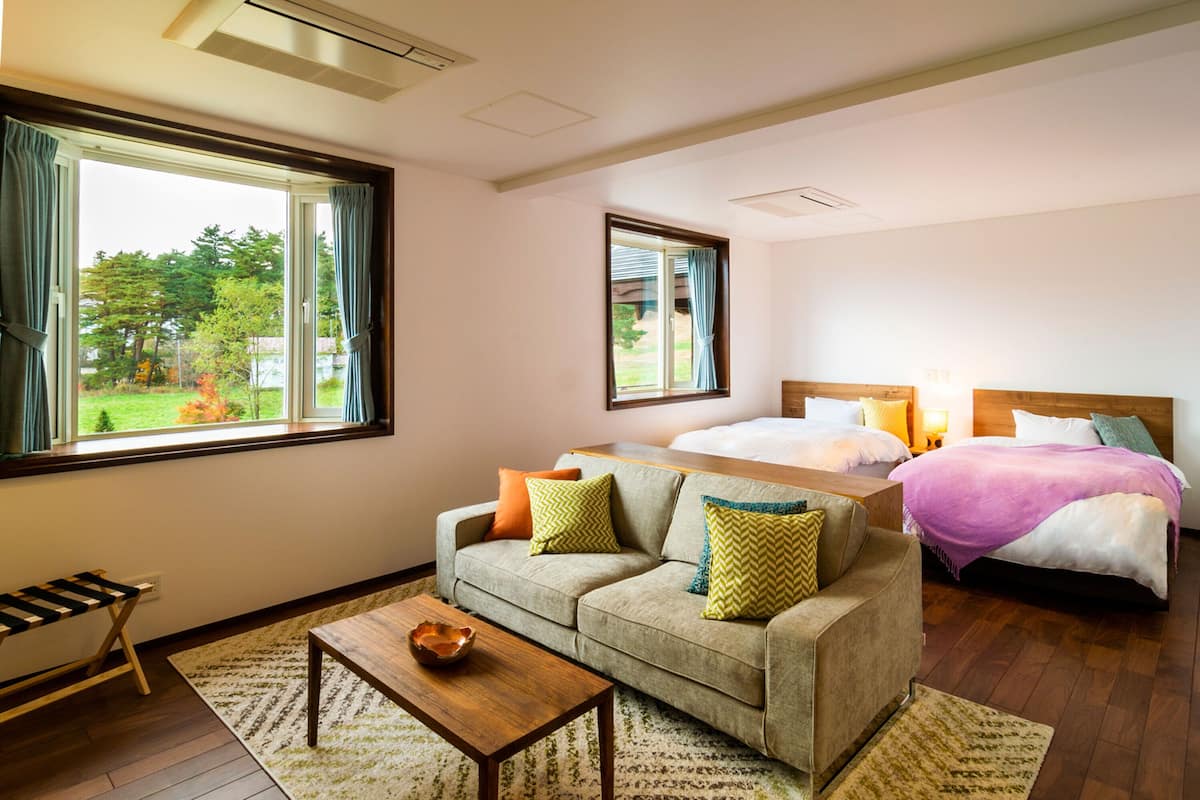 A hotel room with a sofa, a bed, a wooden bench, and a view of the outdoors.