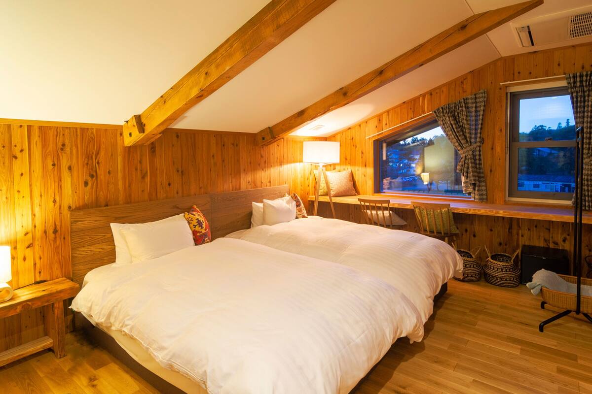 A wooden-paneled bedroom with a large bed, a desk, and a window with curtains.