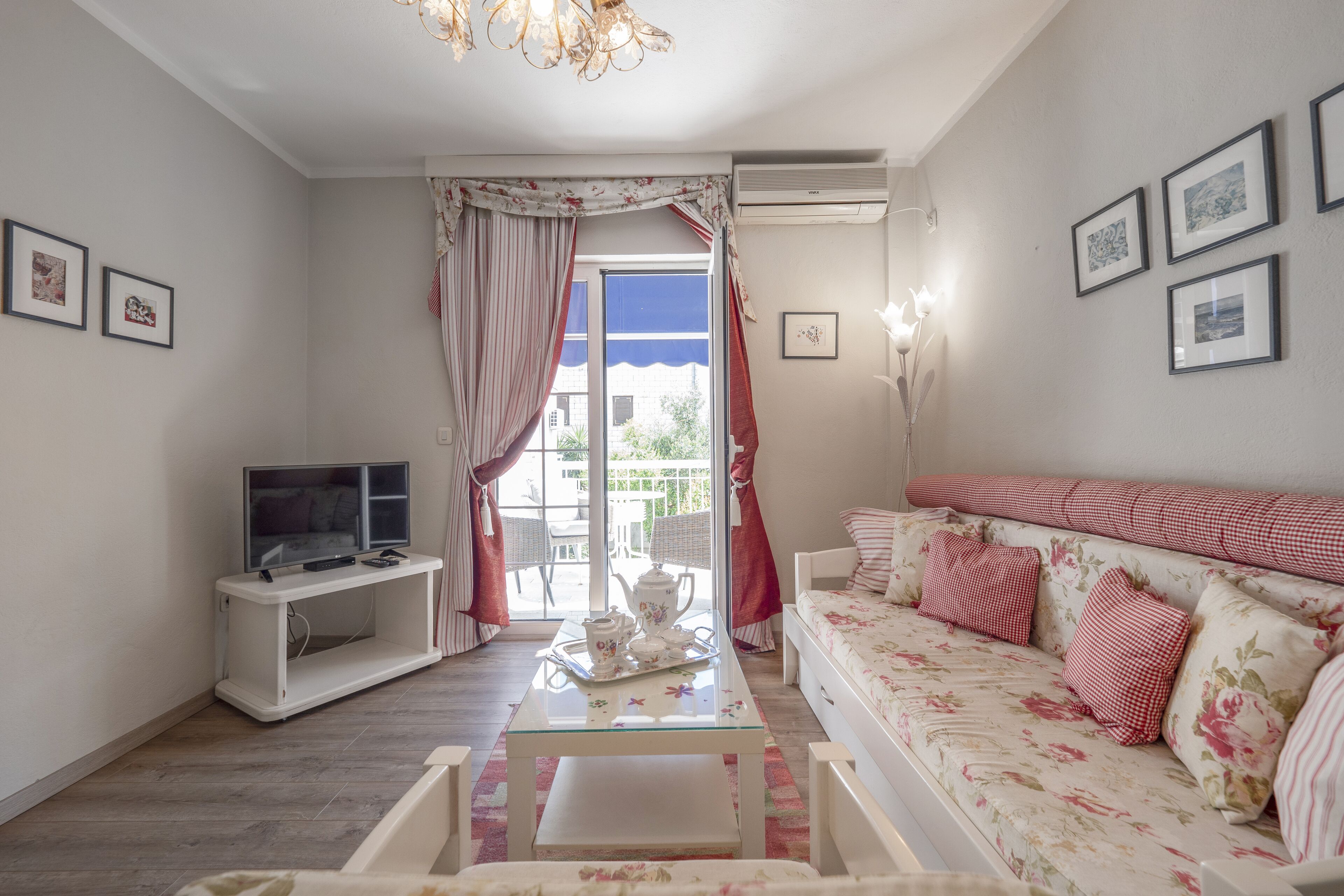 A living room with a sofa, a coffee table, a TV, and a balcony with curtains.