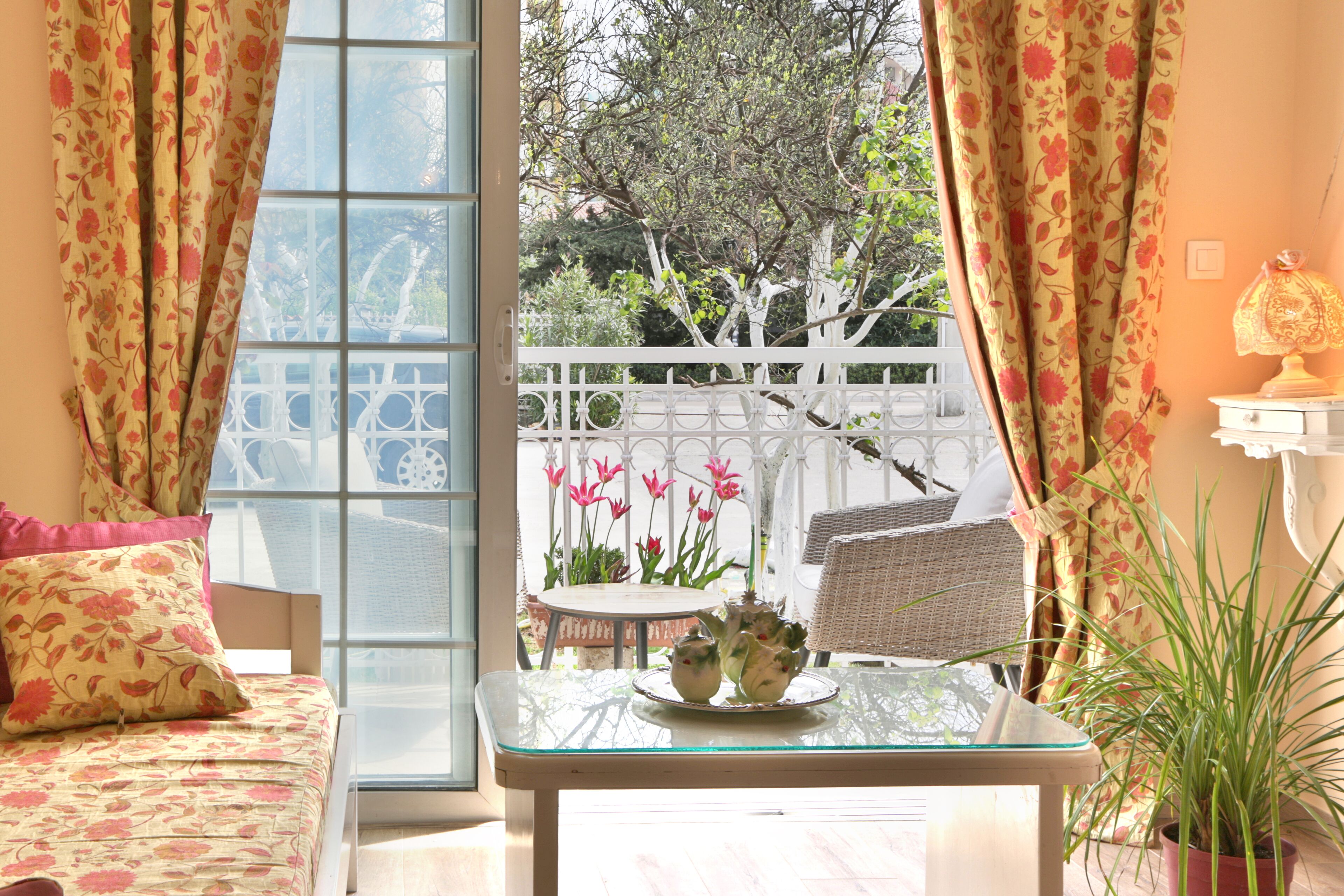 A room with a large window, a glass table with a tray of flowers, a white chair, and a potted plant.