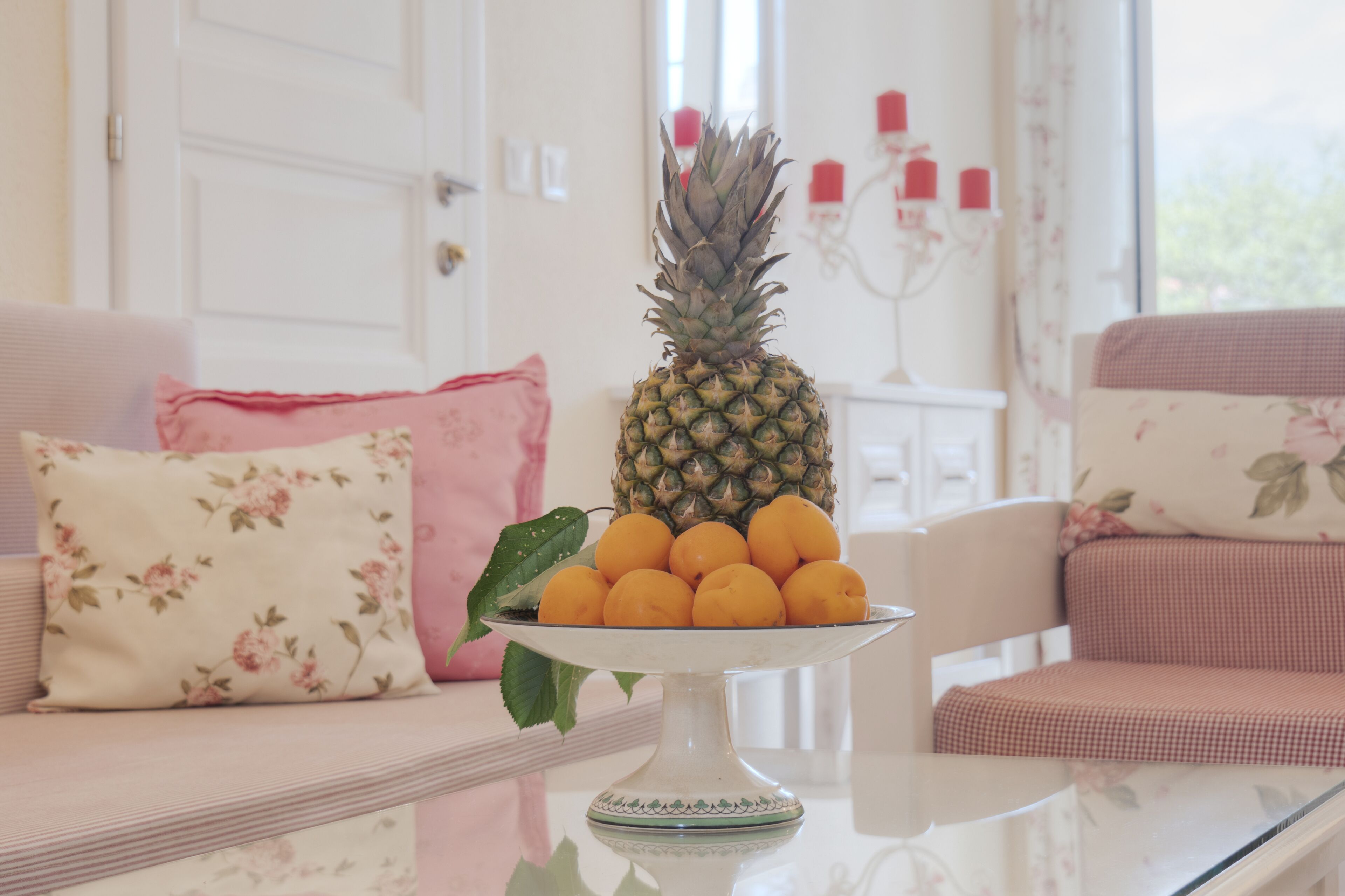 A pineapple and lemons on a white table in a room with floral cushions and a white door.