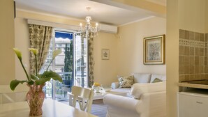 A modern living room with a white sofa, a dining table with a vase of flowers, and a chandelier. - Marinero Apartments (Budva)
