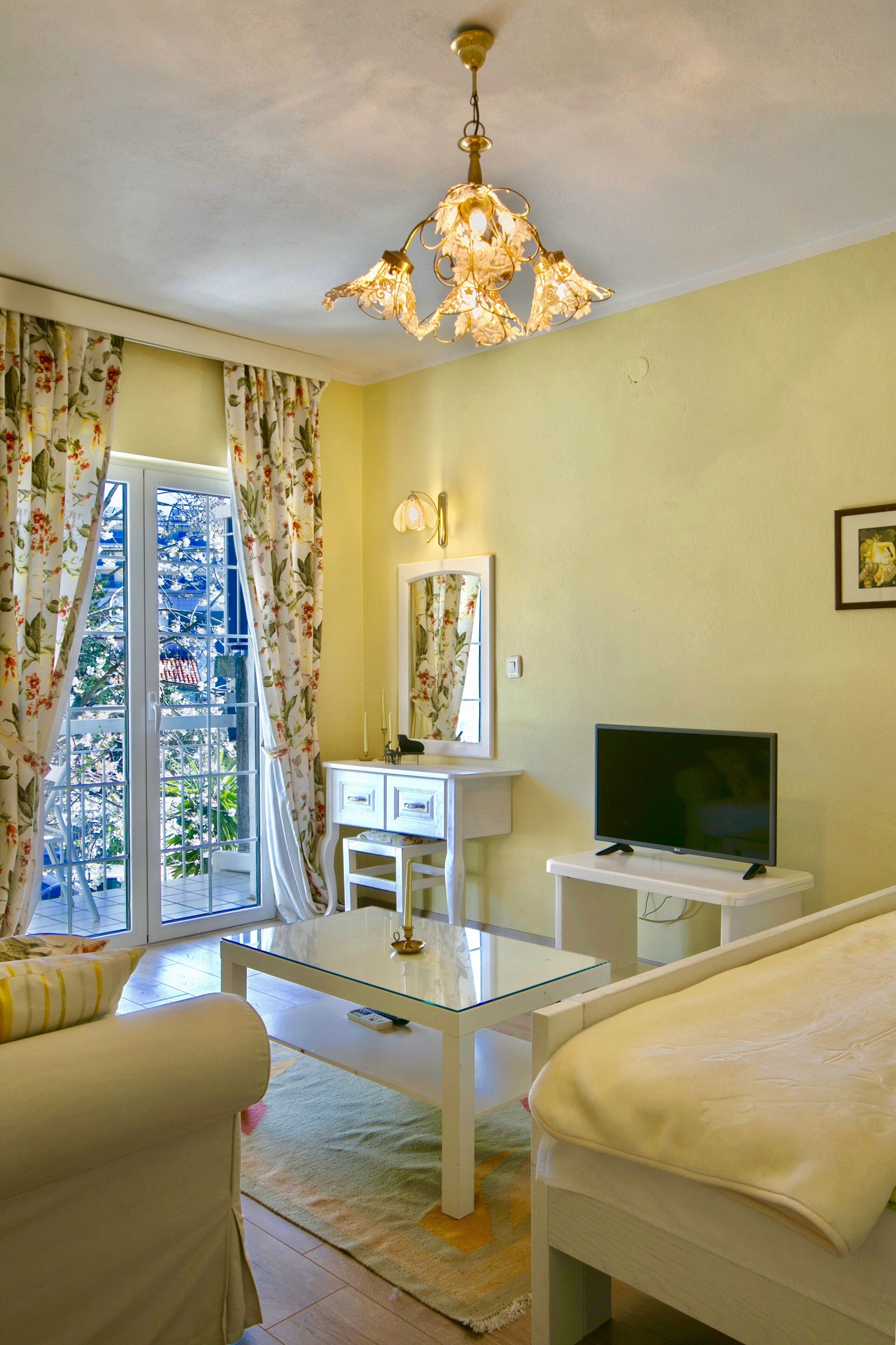 Une chambre à coucher avec un lit, une télévision, une commode, un miroir et une fenêtre avec des rideaux.