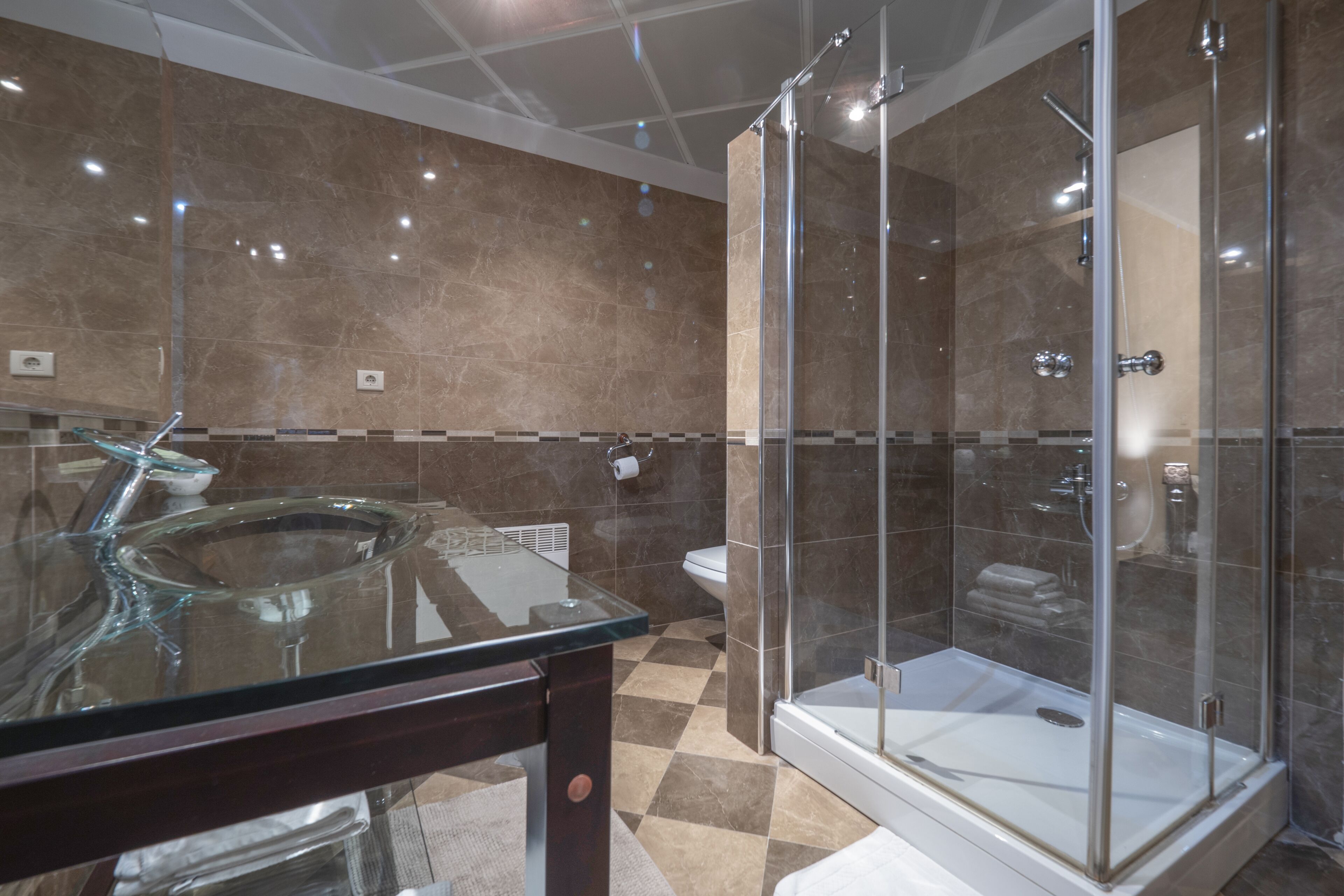 A modern bathroom with a glass sink, a glass-enclosed shower, and a checkered floor.