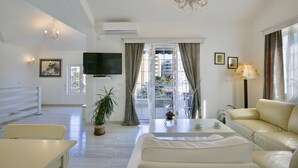 A spacious living room with a sofa, a TV, a chandelier, and a balcony with curtains. - Marinero Apartments (Budva)