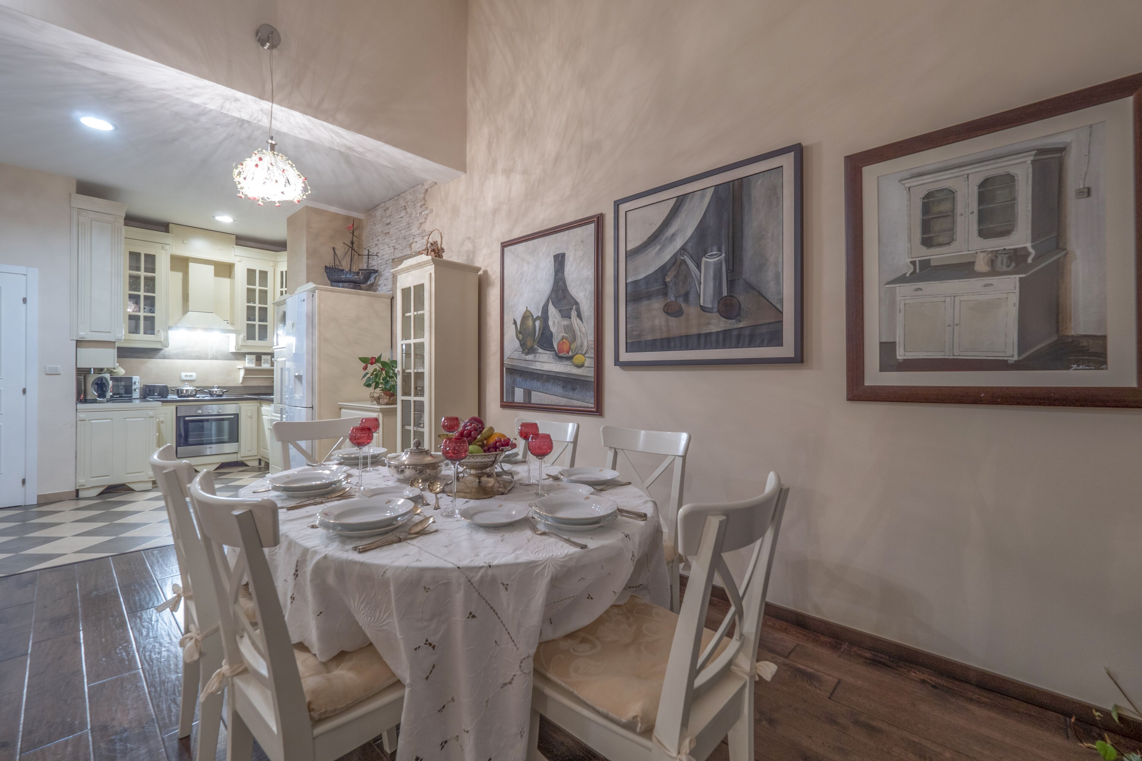 A dining area with a round table set for four, surrounded by white chairs. There are framed artworks on the wall above the table.